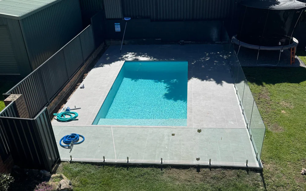 Aerial view of a custom concrete pool with glass fencing and paved surrounds
